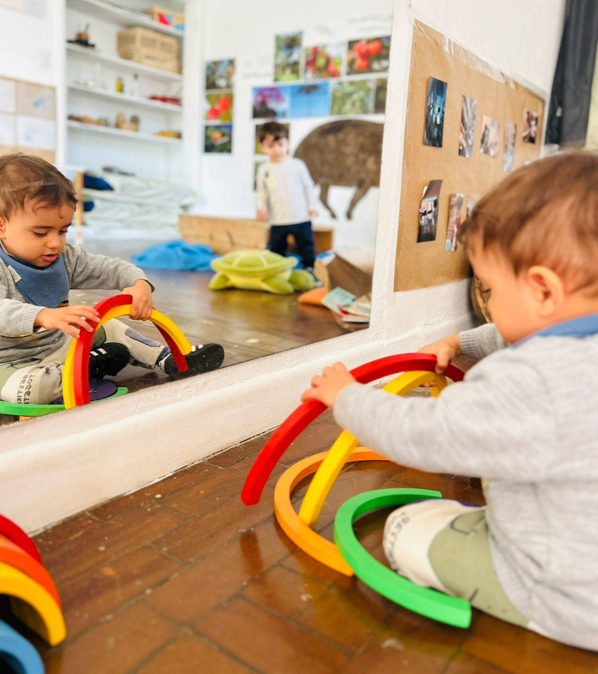 Bebê sentado no chão explorando um arco-íris de madeira em frente ao espelho